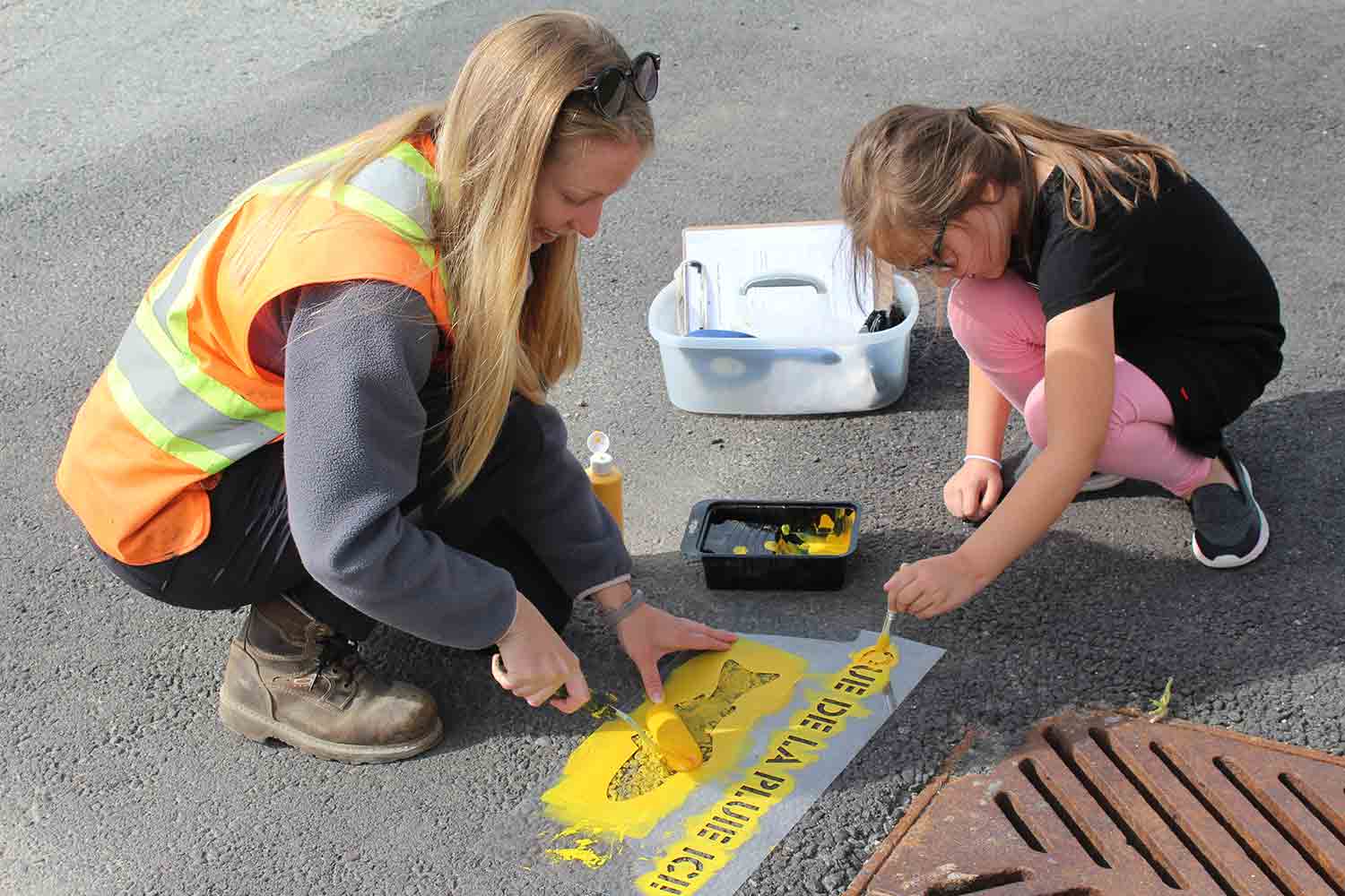 Volunteer and student painting yellow fish near a storm drain